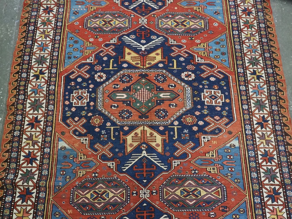 An antique Caucasian Soumak wool flatweave rug featuring three central octagonal medallions surrounded by geometric tribal motifs in red, blue, and yellow. View V