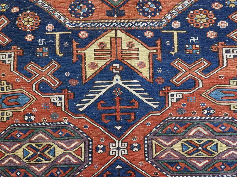 An antique Caucasian Soumak wool flatweave rug featuring three central octagonal medallions surrounded by geometric tribal motifs in red, blue, and yellow. View VI