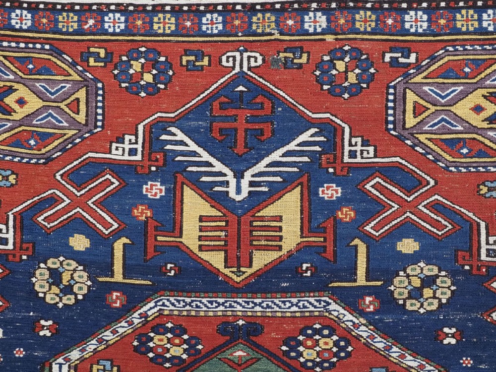 An antique Caucasian Soumak wool flatweave rug featuring three central octagonal medallions surrounded by geometric tribal motifs in red, blue, and yellow. View VII