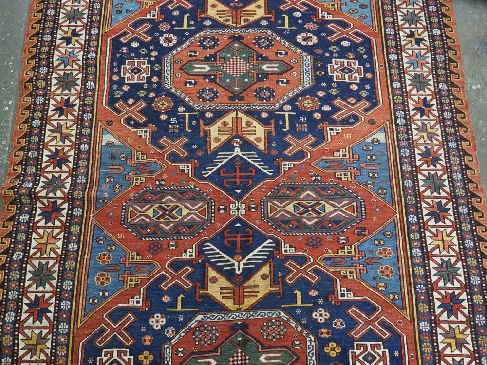 An antique Caucasian Soumak wool flatweave rug featuring three central octagonal medallions surrounded by geometric tribal motifs in red, blue, and yellow. View IX