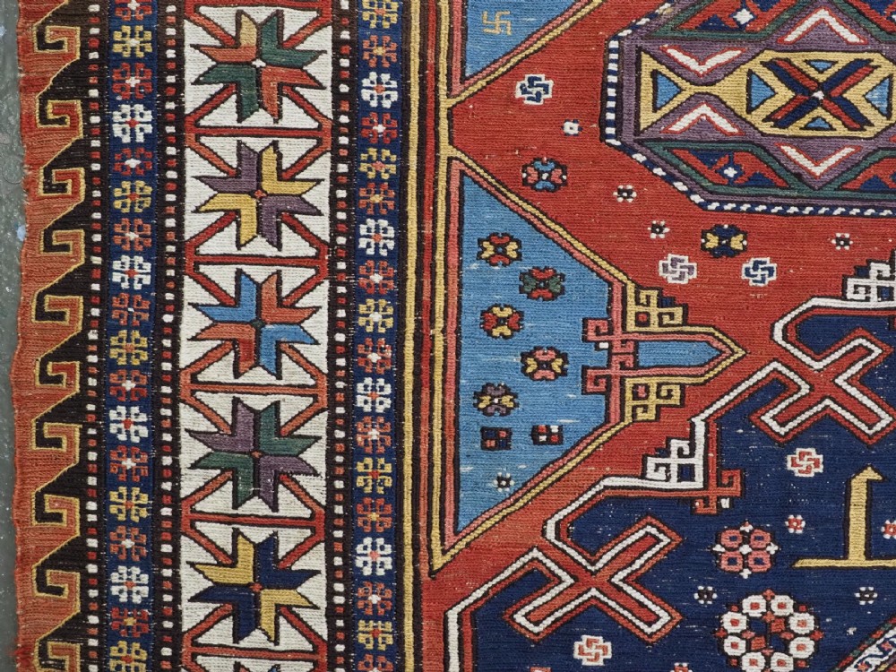 An antique Caucasian Soumak wool flatweave rug featuring three central octagonal medallions surrounded by geometric tribal motifs in red, blue, and yellow. View X