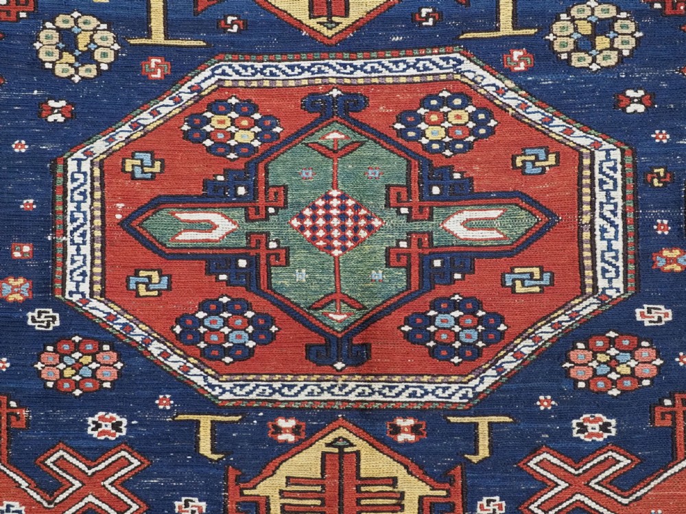 An antique Caucasian Soumak wool flatweave rug featuring three central octagonal medallions surrounded by geometric tribal motifs in red, blue, and yellow. View XI