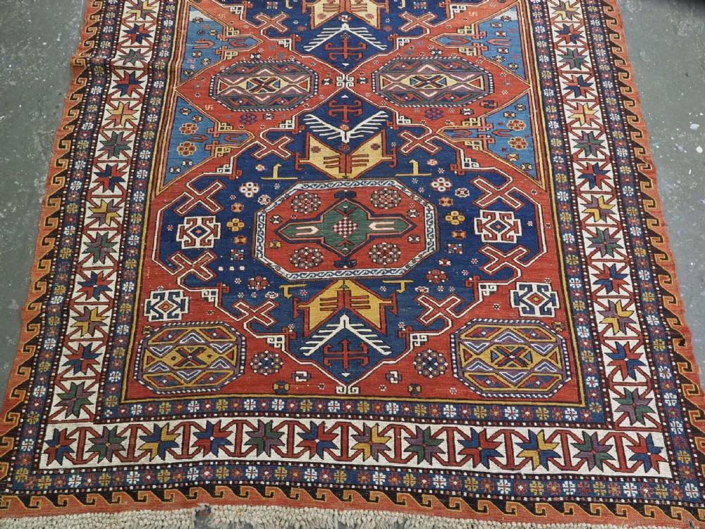 An antique Caucasian Soumak wool flatweave rug featuring three central octagonal medallions surrounded by geometric tribal motifs in red, blue, and yellow. View XIII