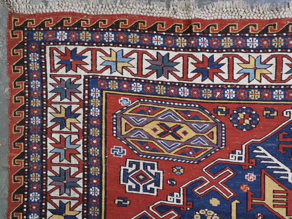 An antique Caucasian Soumak wool flatweave rug featuring three central octagonal medallions surrounded by geometric tribal motifs in red, blue, and yellow. View XIV