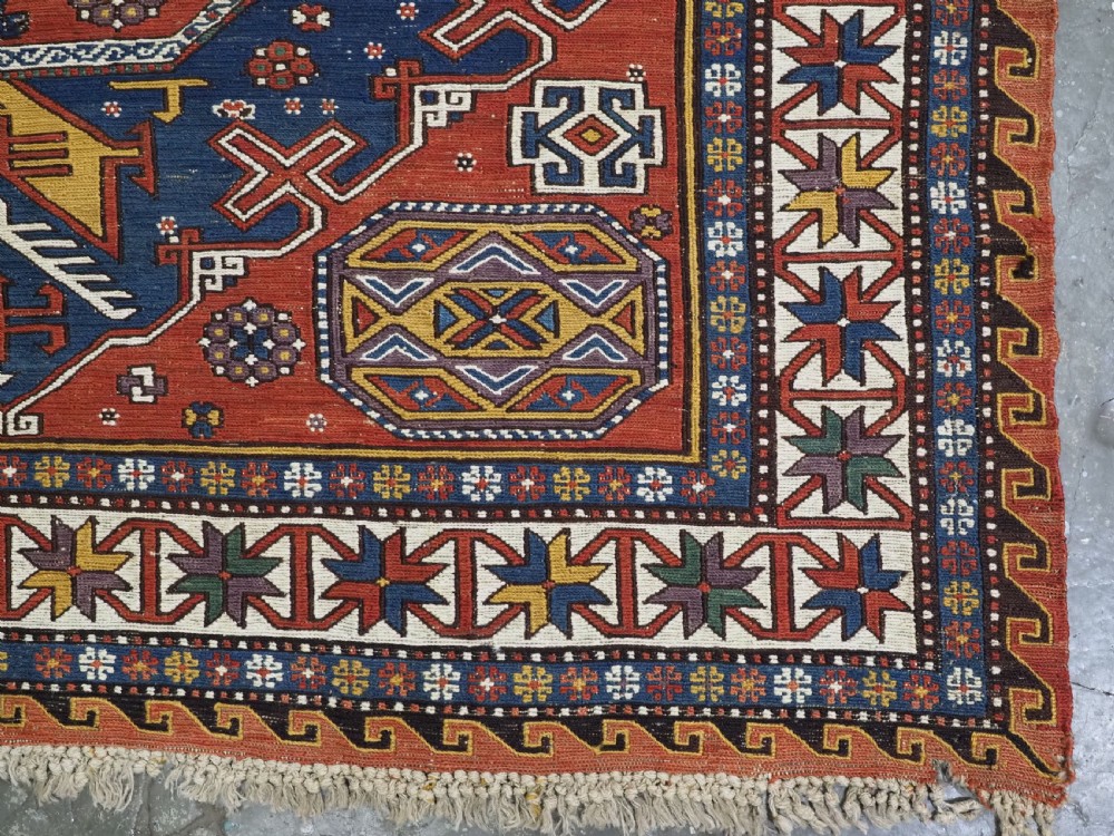 An antique Caucasian Soumak wool flatweave rug featuring three central octagonal medallions surrounded by geometric tribal motifs in red, blue, and yellow. View XV