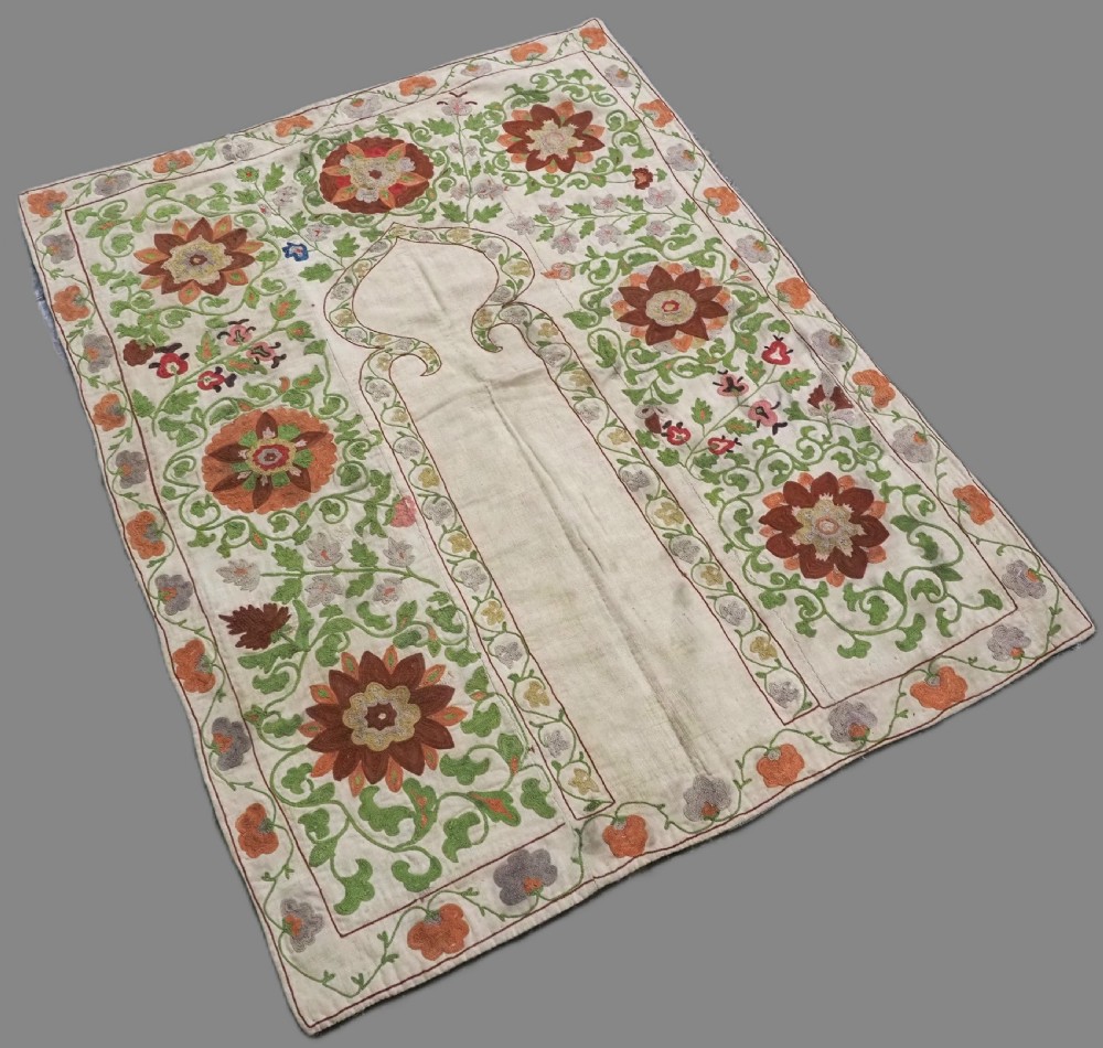 A cream woven cotton textile panel decorated with intricate silk embroidery depicting a pointed arch niche surrounded by floral rosettes and vine tendrils in terracotta and green tones. View II
