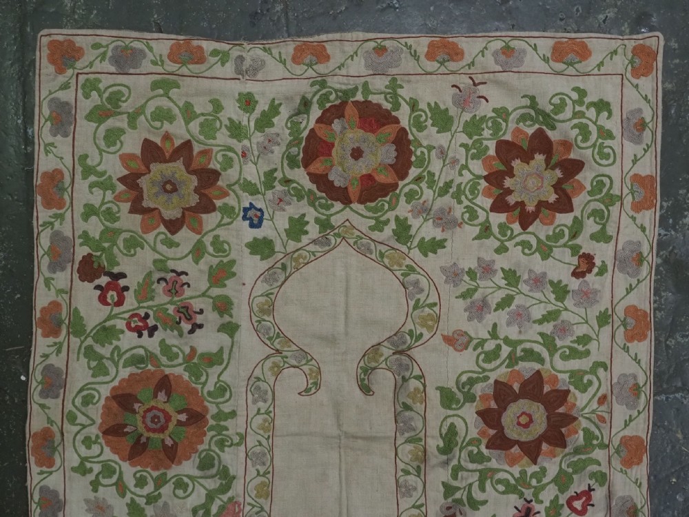 A cream woven cotton textile panel decorated with intricate silk embroidery depicting a pointed arch niche surrounded by floral rosettes and vine tendrils in terracotta and green tones. View III