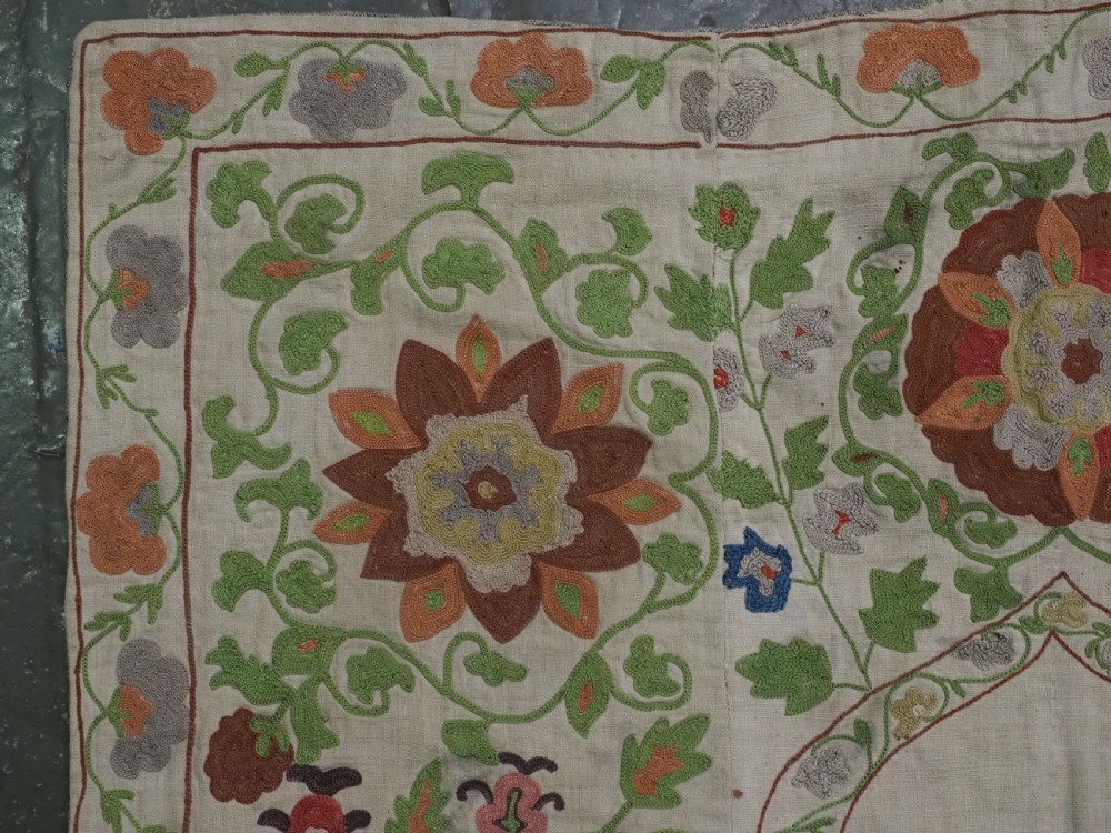 A cream woven cotton textile panel decorated with intricate silk embroidery depicting a pointed arch niche surrounded by floral rosettes and vine tendrils in terracotta and green tones. View V