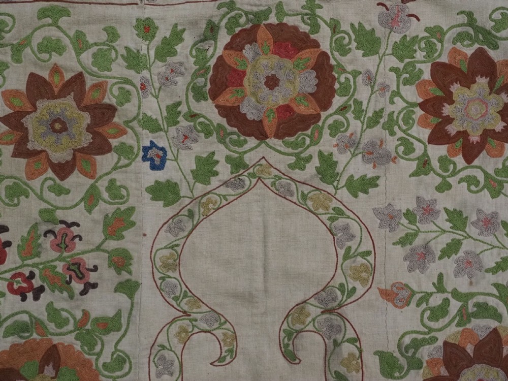 A cream woven cotton textile panel decorated with intricate silk embroidery depicting a pointed arch niche surrounded by floral rosettes and vine tendrils in terracotta and green tones. View VI