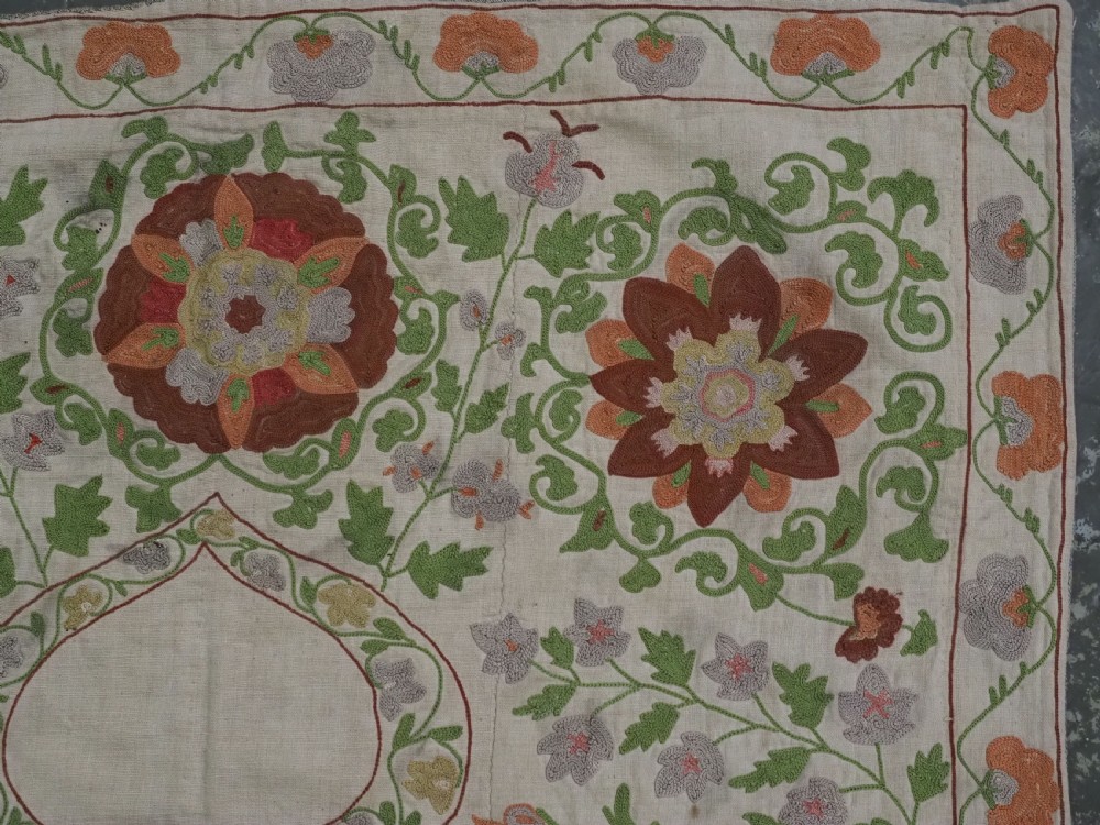 A cream woven cotton textile panel decorated with intricate silk embroidery depicting a pointed arch niche surrounded by floral rosettes and vine tendrils in terracotta and green tones. View VII