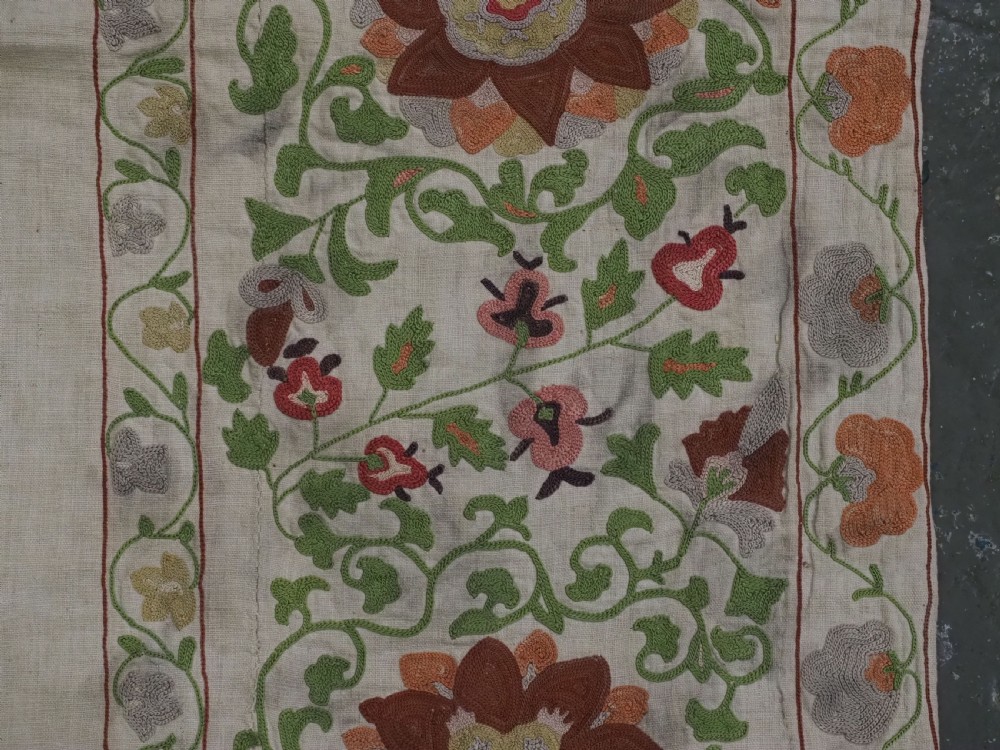 A cream woven cotton textile panel decorated with intricate silk embroidery depicting a pointed arch niche surrounded by floral rosettes and vine tendrils in terracotta and green tones. View IX