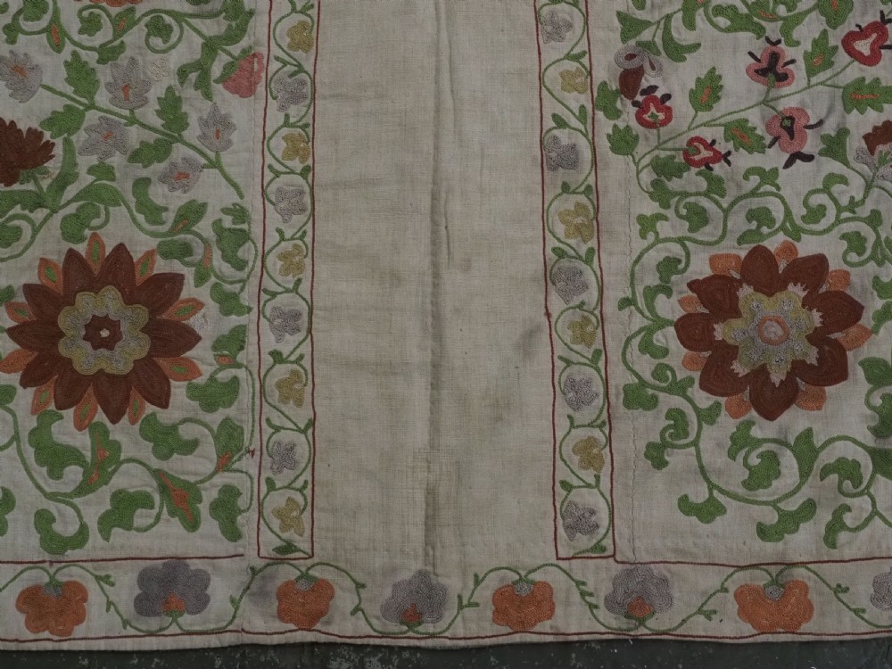 A cream woven cotton textile panel decorated with intricate silk embroidery depicting a pointed arch niche surrounded by floral rosettes and vine tendrils in terracotta and green tones. View X