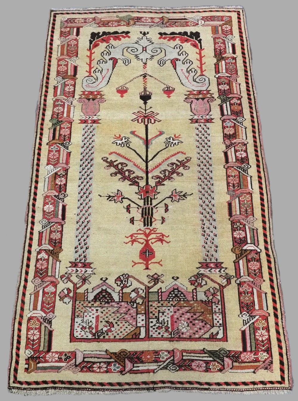 An antique Turkish Kirsehir wool prayer rug featuring a cream central field with a pointed mihrab niche, central tree of life motif, and geometric floral borders in muted red, pink, and green tones.