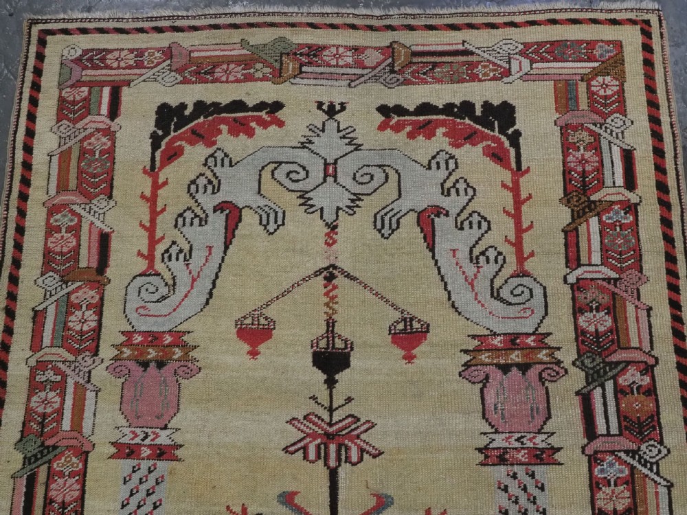 An antique Turkish Kirsehir wool prayer rug featuring a cream central field with a pointed mihrab niche, central tree of life motif, and geometric floral borders in muted red, pink, and green tones. View III