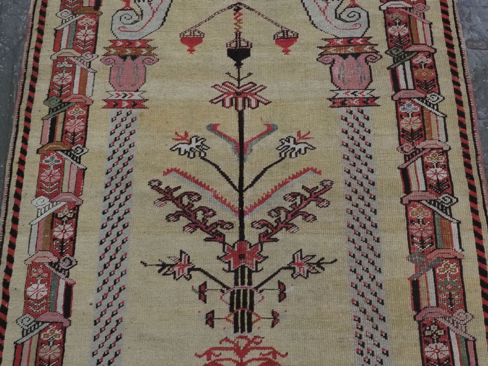 An antique Turkish Kirsehir wool prayer rug featuring a cream central field with a pointed mihrab niche, central tree of life motif, and geometric floral borders in muted red, pink, and green tones. View IV