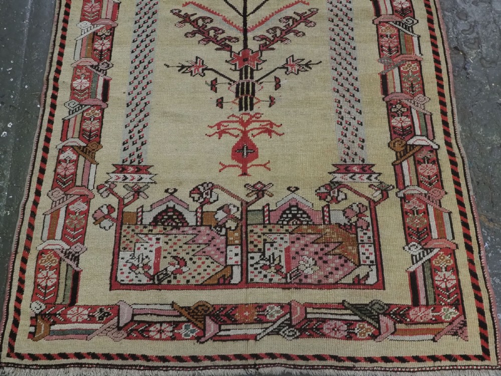 An antique Turkish Kirsehir wool prayer rug featuring a cream central field with a pointed mihrab niche, central tree of life motif, and geometric floral borders in muted red, pink, and green tones. View V