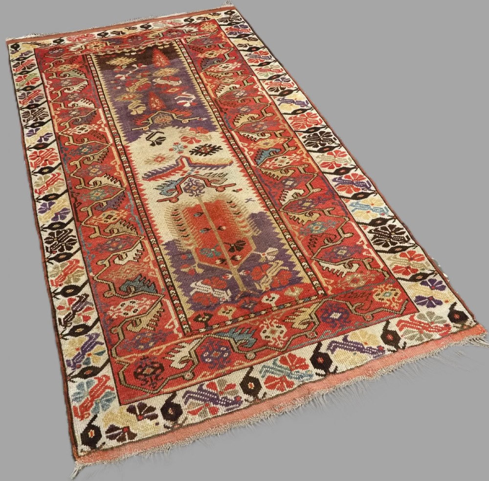 An antique hand-knotted Turkish Milas wool prayer rug featuring a central ivory prayer niche flanked by geometric borders in terracotta, purple, and cream tones. View II
