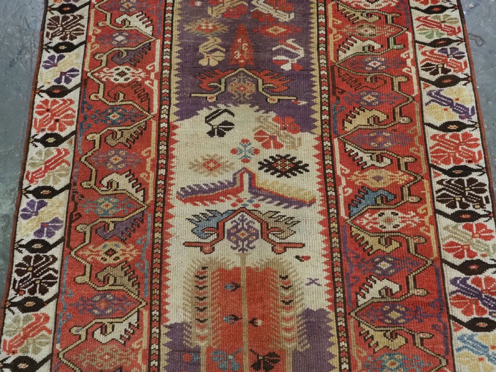 An antique hand-knotted Turkish Milas wool prayer rug featuring a central ivory prayer niche flanked by geometric borders in terracotta, purple, and cream tones. View III