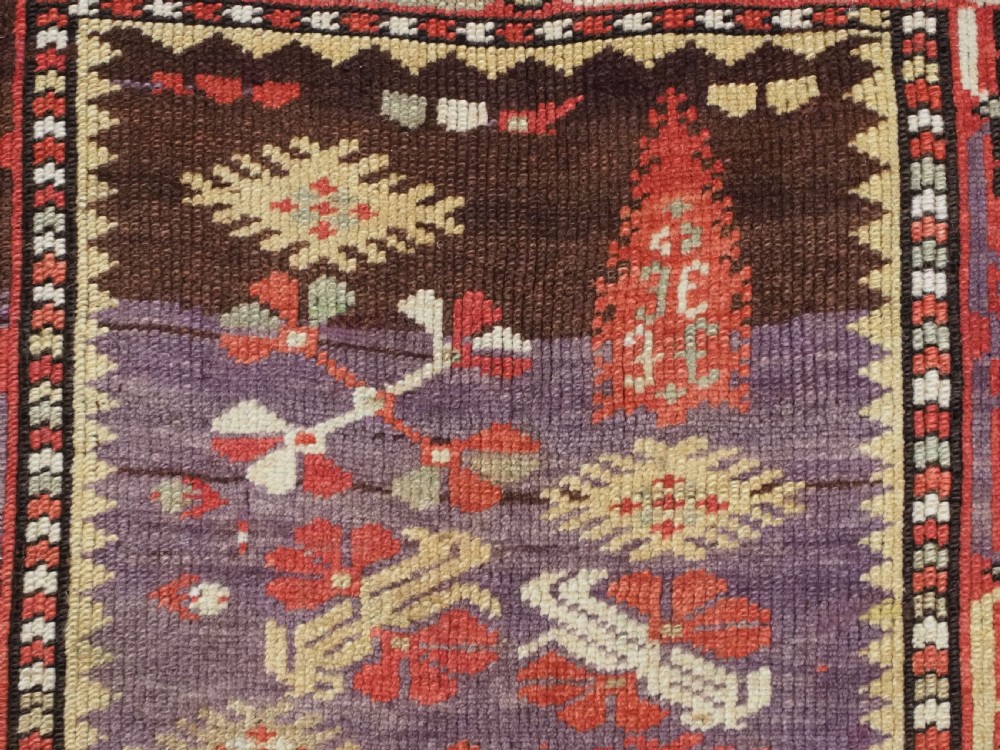 An antique hand-knotted Turkish Milas wool prayer rug featuring a central ivory prayer niche flanked by geometric borders in terracotta, purple, and cream tones. View VIII