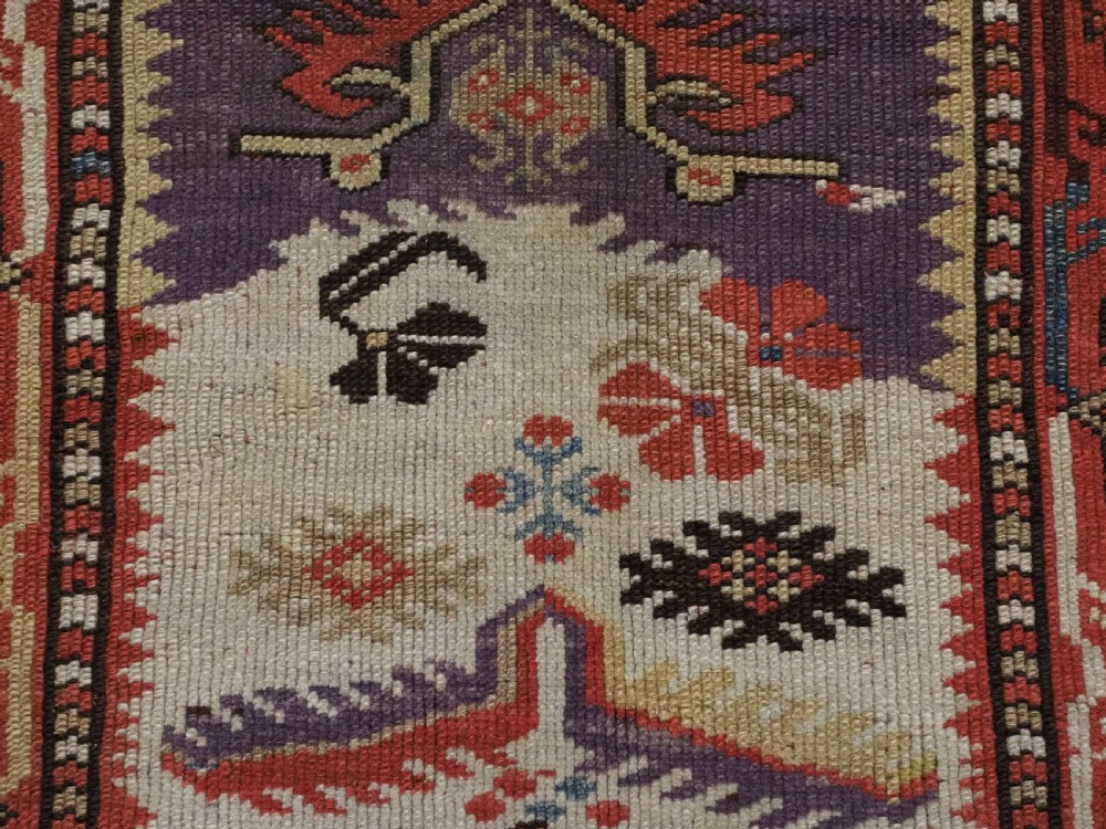 An antique hand-knotted Turkish Milas wool prayer rug featuring a central ivory prayer niche flanked by geometric borders in terracotta, purple, and cream tones. View IX