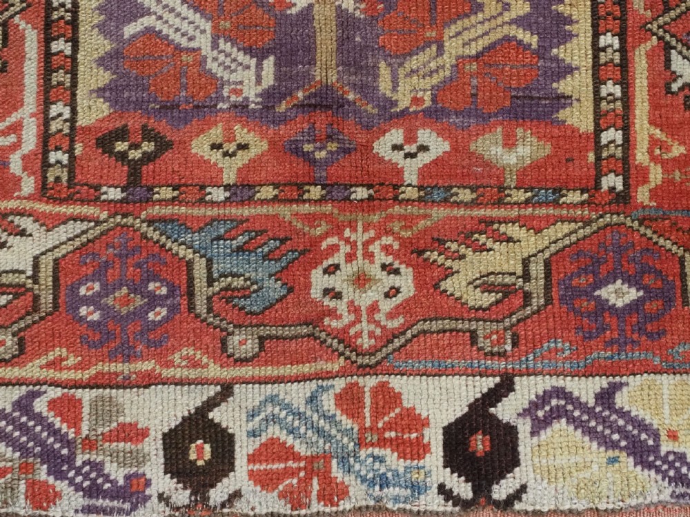 An antique hand-knotted Turkish Milas wool prayer rug featuring a central ivory prayer niche flanked by geometric borders in terracotta, purple, and cream tones. View XI
