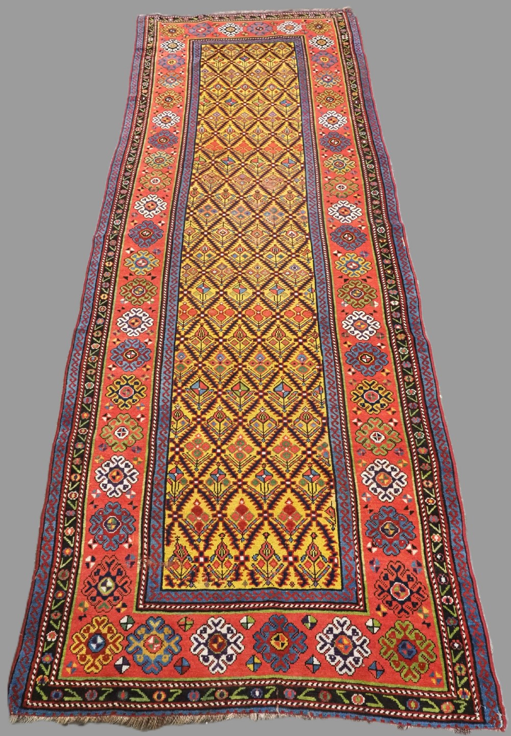 An antique long hand-knotted wool runner rug featuring a yellow lattice pattern field framed by wide red floral geometric borders.