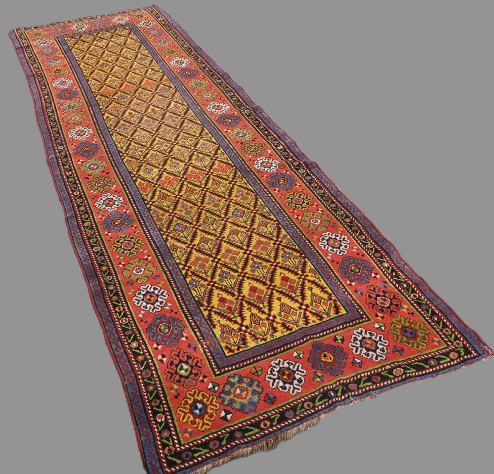An antique long hand-knotted wool runner rug featuring a yellow lattice pattern field framed by wide red floral geometric borders. View II