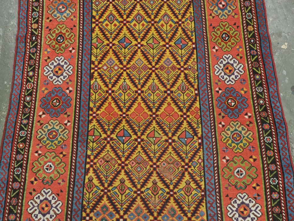 An antique long hand-knotted wool runner rug featuring a yellow lattice pattern field framed by wide red floral geometric borders. View IV