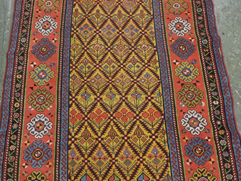 An antique long hand-knotted wool runner rug featuring a yellow lattice pattern field framed by wide red floral geometric borders. View V