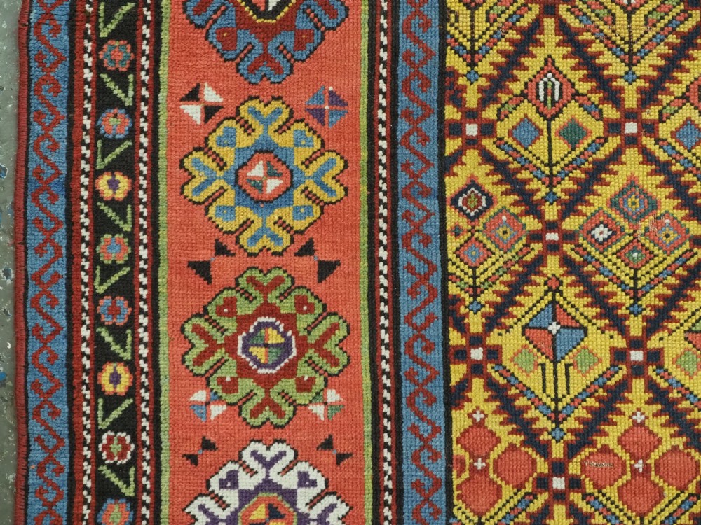 An antique long hand-knotted wool runner rug featuring a yellow lattice pattern field framed by wide red floral geometric borders. View VIII