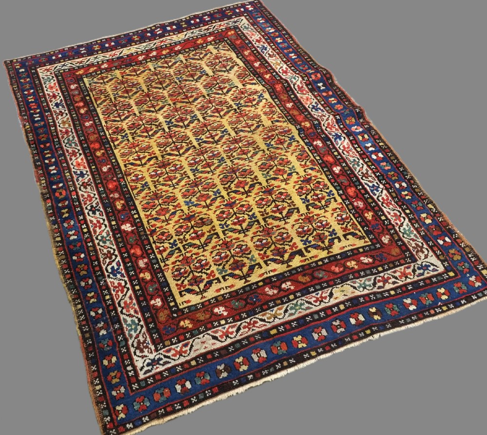 An antique hand-knotted Kurdish wool rug featuring a bright yellow central field with repeating red and blue shrub motifs enclosed within patterned borders. View II