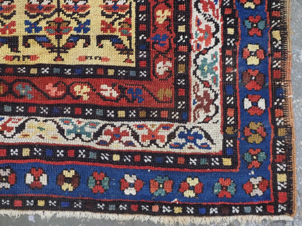 An antique hand-knotted Kurdish wool rug featuring a bright yellow central field with repeating red and blue shrub motifs enclosed within patterned borders. View XI