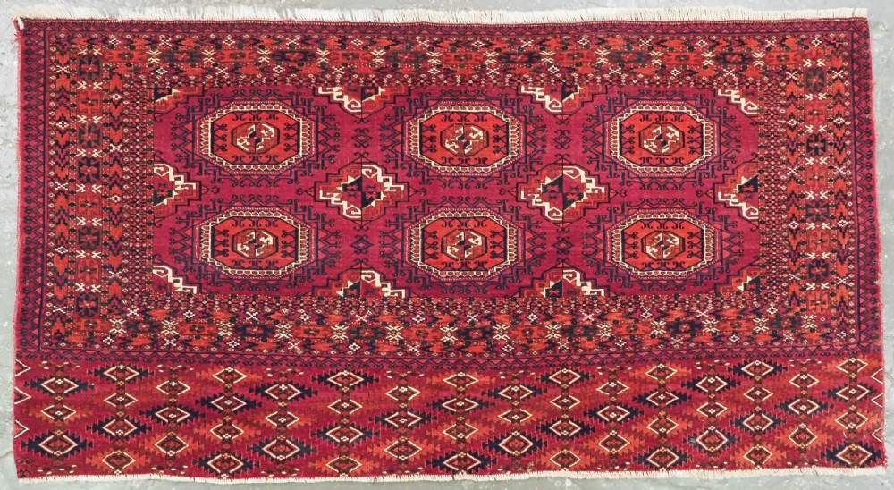 A hand-knotted deep red wool Turkmen chuval face featuring six octagonal Salor guls and a geometric bottom elem border.