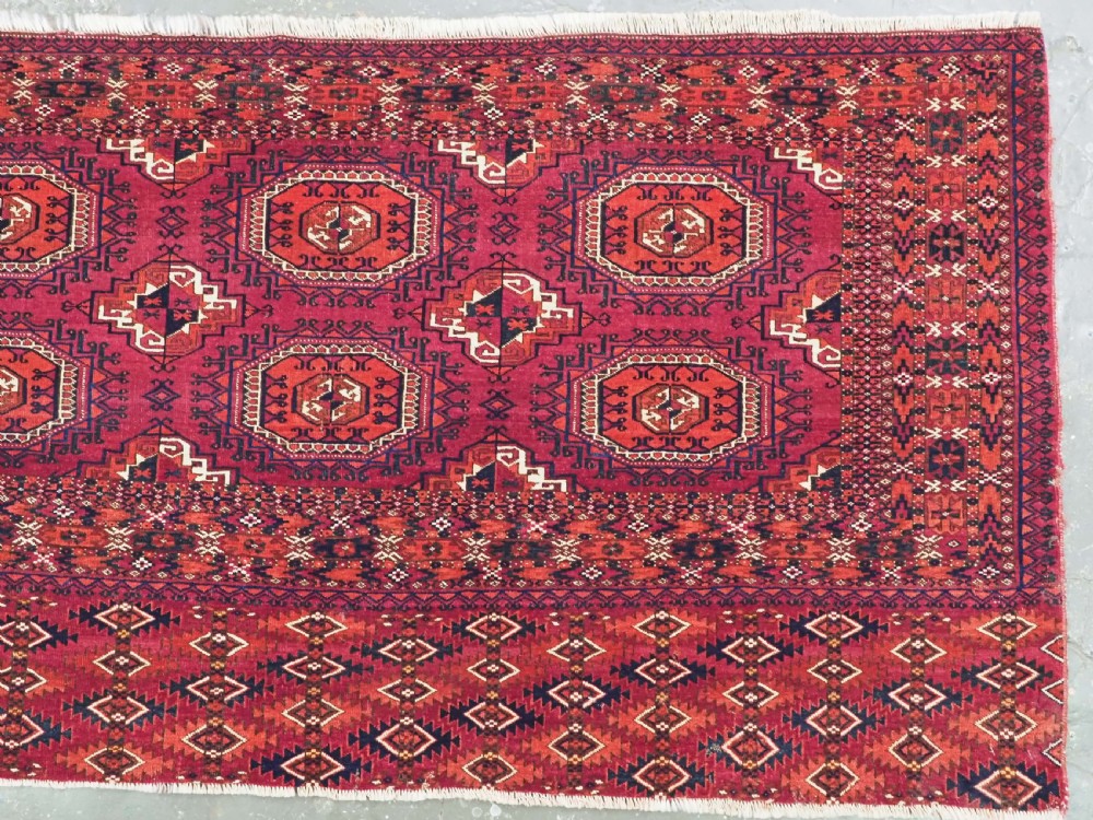 A hand-knotted deep red wool Turkmen chuval face featuring six octagonal Salor guls and a geometric bottom elem border. View IV