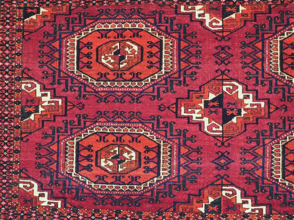 A hand-knotted deep red wool Turkmen chuval face featuring six octagonal Salor guls and a geometric bottom elem border. View VI