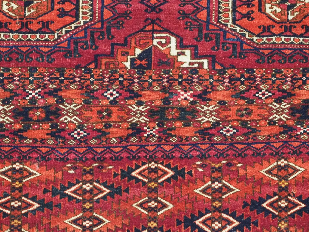 A hand-knotted deep red wool Turkmen chuval face featuring six octagonal Salor guls and a geometric bottom elem border. View IX
