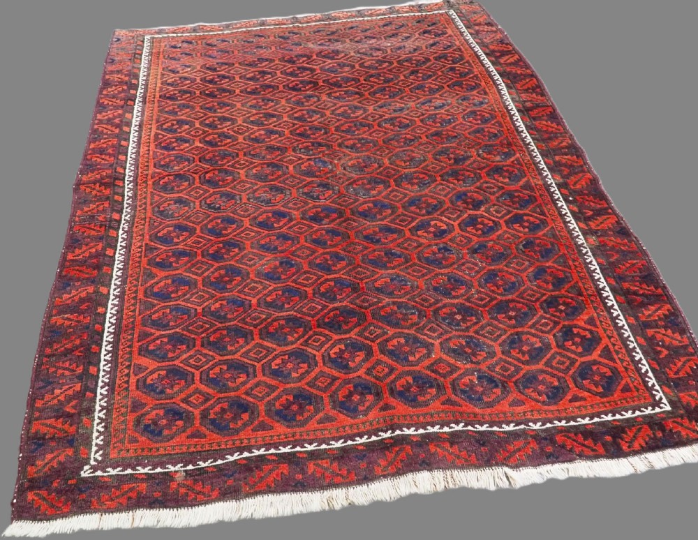 An antique hand-knotted wool Baluch rug featuring a repeating star in octagon pattern in dark red, indigo, and brown tones with a white inner border. View II