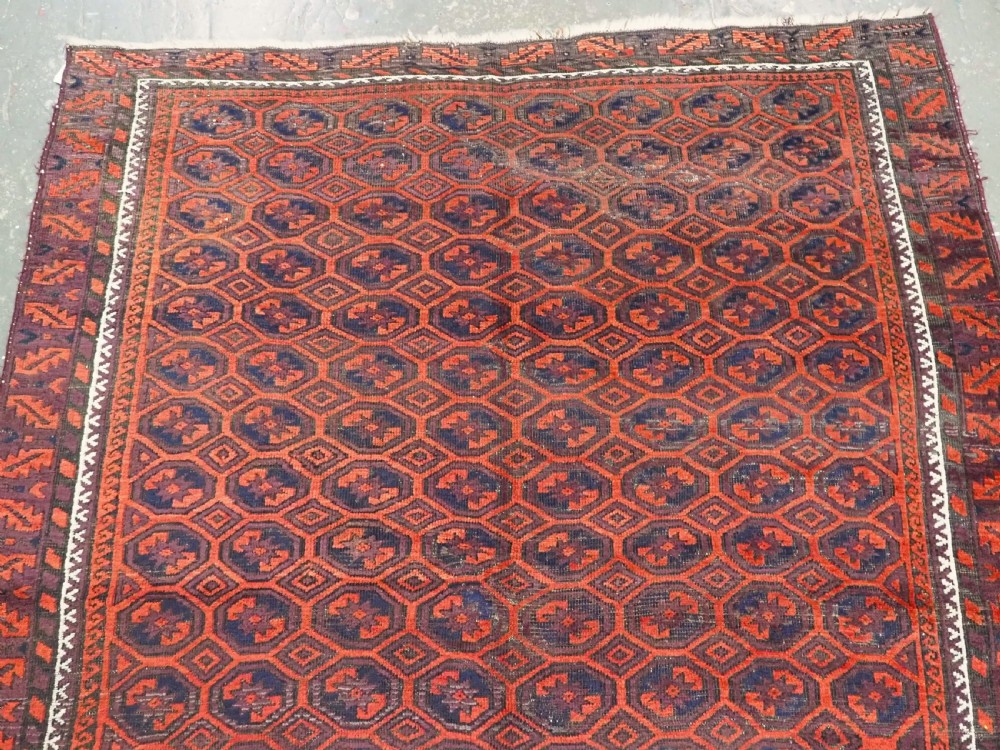An antique hand-knotted wool Baluch rug featuring a repeating star in octagon pattern in dark red, indigo, and brown tones with a white inner border. View III