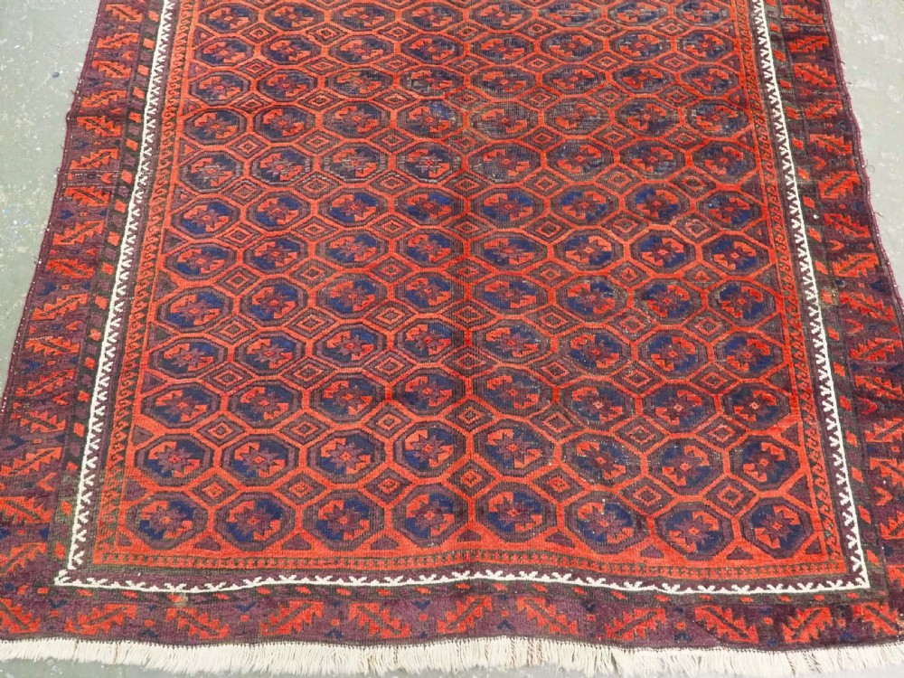 An antique hand-knotted wool Baluch rug featuring a repeating star in octagon pattern in dark red, indigo, and brown tones with a white inner border. View IV