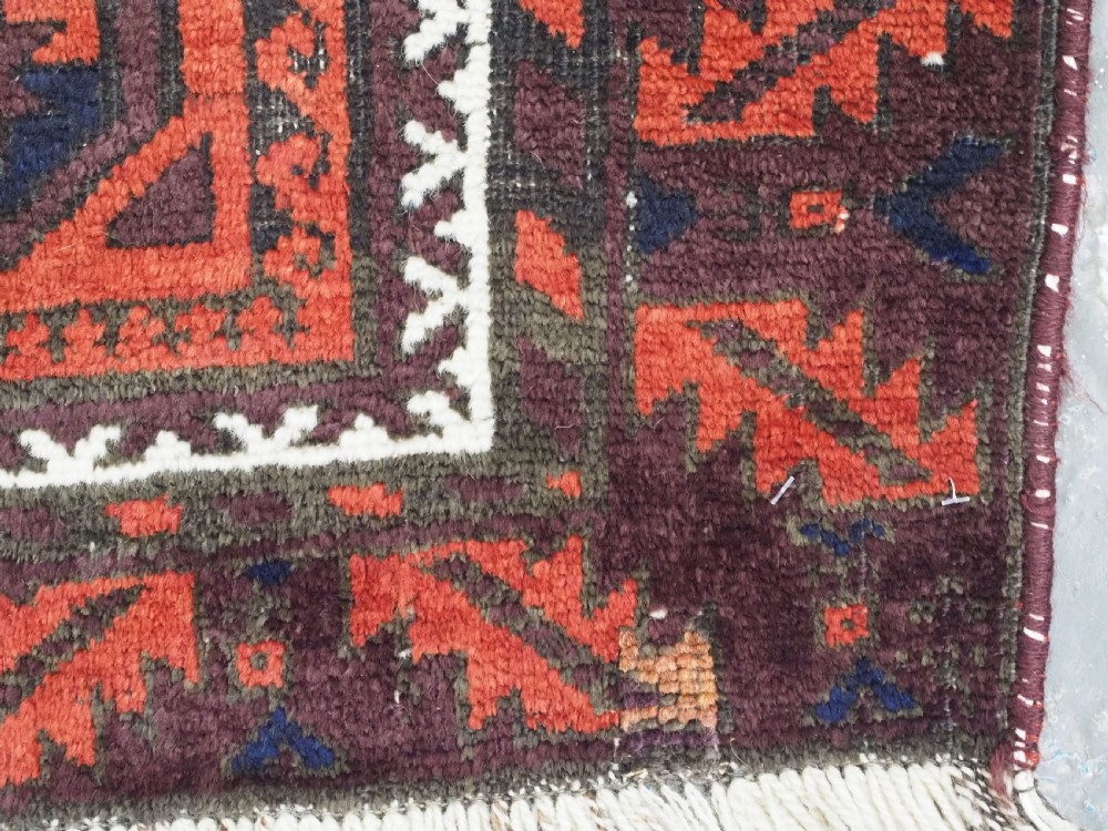 An antique hand-knotted wool Baluch rug featuring a repeating star in octagon pattern in dark red, indigo, and brown tones with a white inner border. View V