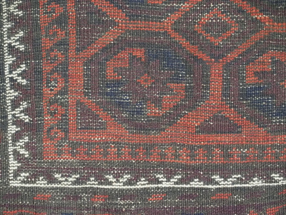 An antique hand-knotted wool Baluch rug featuring a repeating star in octagon pattern in dark red, indigo, and brown tones with a white inner border. View VI