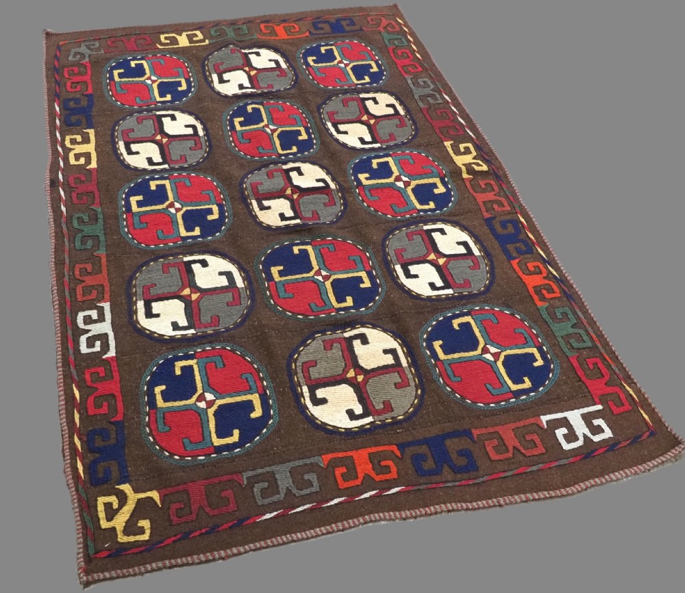 An antique brown camel hair flatweave kilim rug featuring fifteen circular embroidered medallions filled with colourful geometric motifs within a decorative hooked border. View II