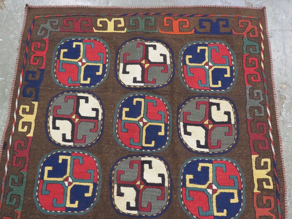 An antique brown camel hair flatweave kilim rug featuring fifteen circular embroidered medallions filled with colourful geometric motifs within a decorative hooked border. View III