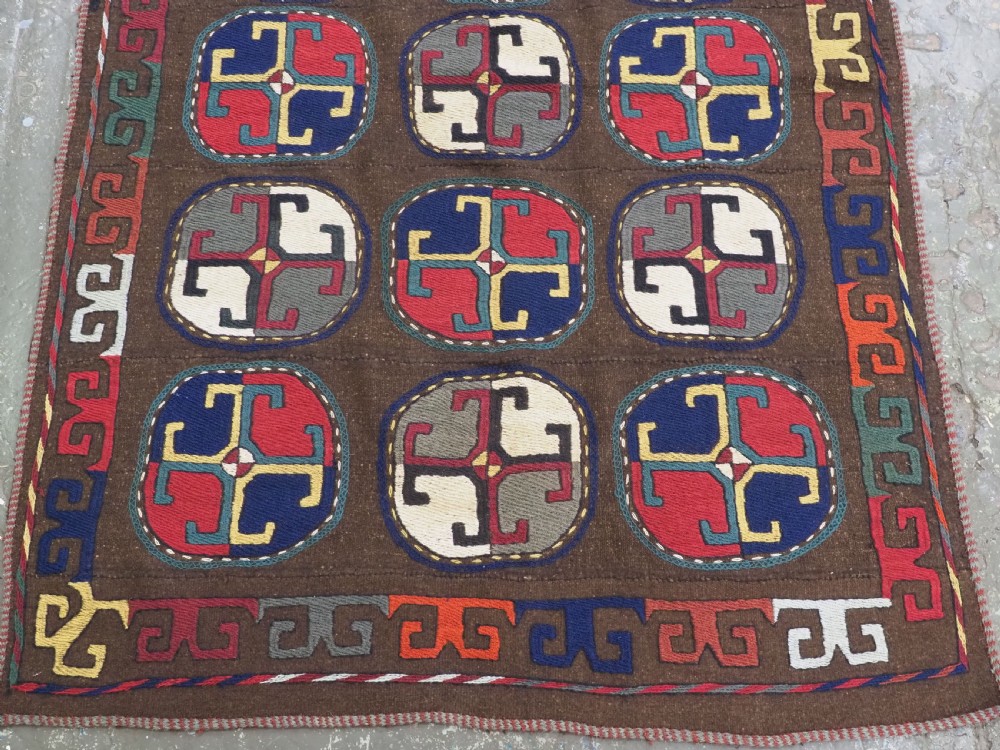 An antique brown camel hair flatweave kilim rug featuring fifteen circular embroidered medallions filled with colourful geometric motifs within a decorative hooked border. View IV