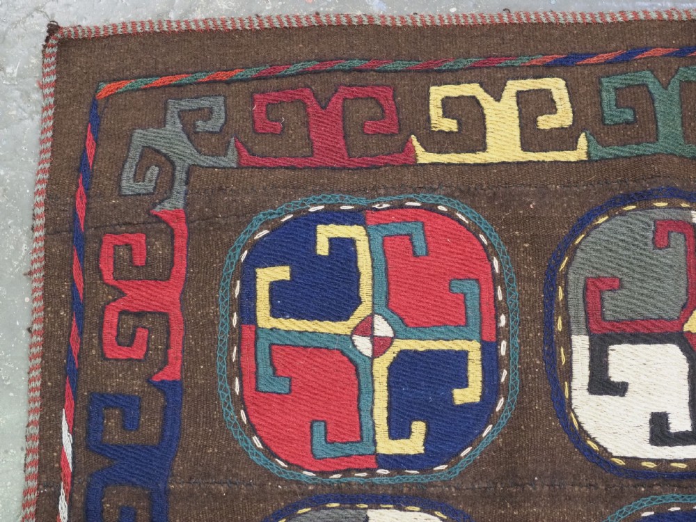 An antique brown camel hair flatweave kilim rug featuring fifteen circular embroidered medallions filled with colourful geometric motifs within a decorative hooked border. View V