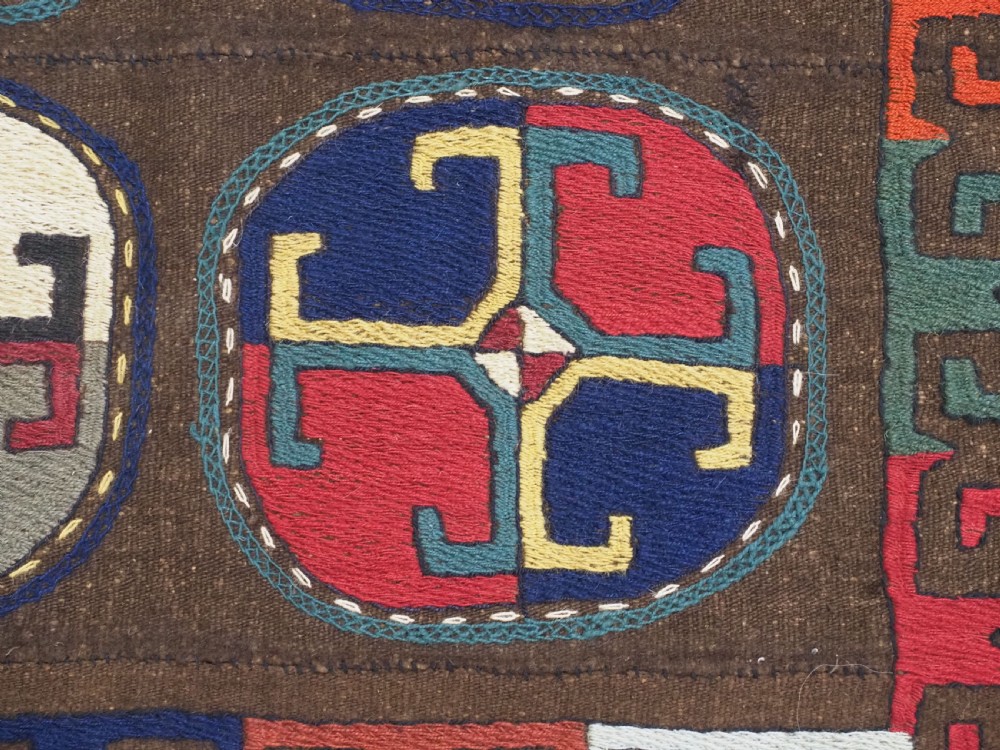 An antique brown camel hair flatweave kilim rug featuring fifteen circular embroidered medallions filled with colourful geometric motifs within a decorative hooked border. View IX