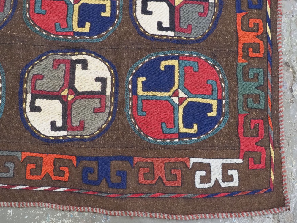 An antique brown camel hair flatweave kilim rug featuring fifteen circular embroidered medallions filled with colourful geometric motifs within a decorative hooked border. View X
