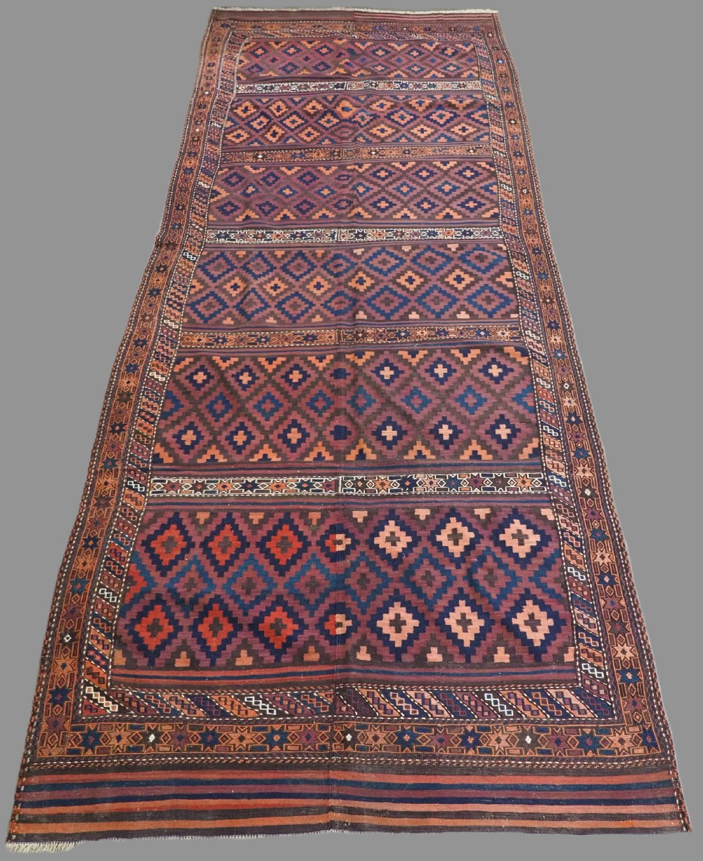A large flatweave Baluch wool kilim rug featuring two joined panels with geometric diamond bands in terracotta, indigo, and dark brown hues.