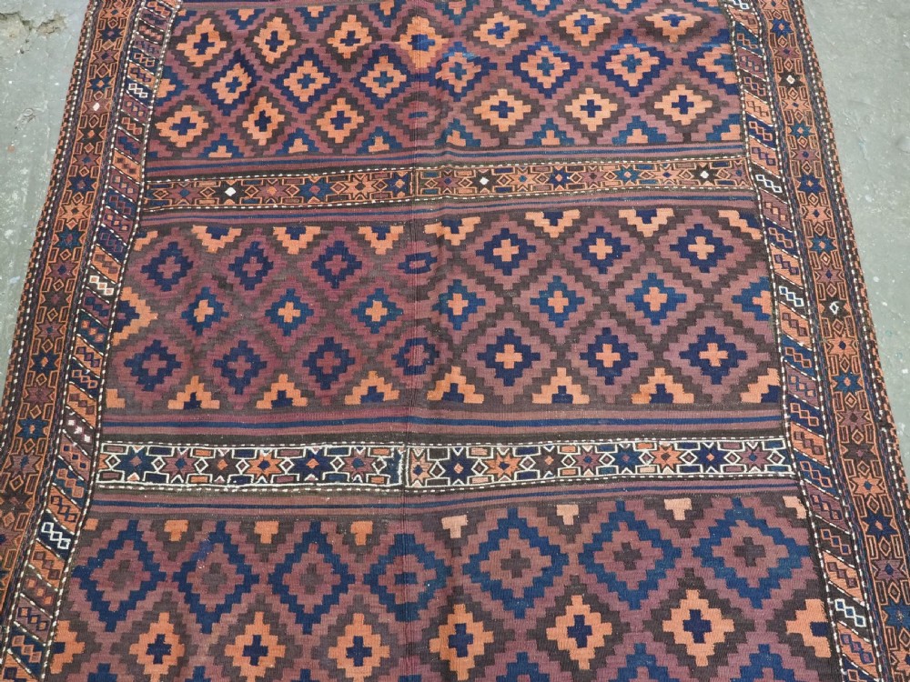 A large flatweave Baluch wool kilim rug featuring two joined panels with geometric diamond bands in terracotta, indigo, and dark brown hues. View IV