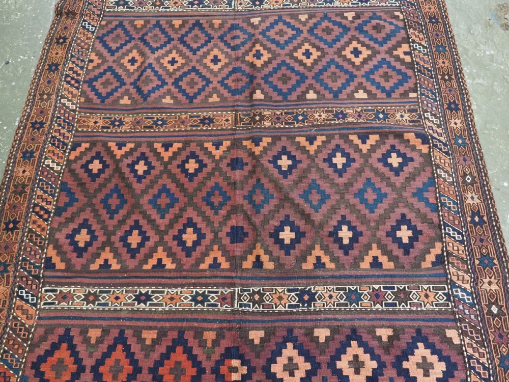 A large flatweave Baluch wool kilim rug featuring two joined panels with geometric diamond bands in terracotta, indigo, and dark brown hues. View V